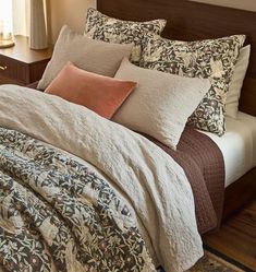 a bed with several pillows and blankets on it in a bedroom area next to a window