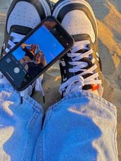 a person's feet with sneakers and a cell phone in their lap on the beach