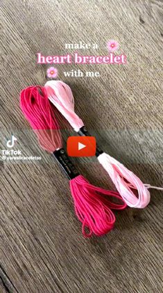 two pink and white tassels on top of a wooden floor with text that reads make a heart bracelet with me