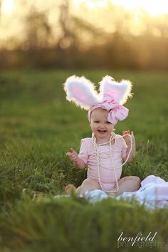 a baby sitting in the grass wearing bunny ears