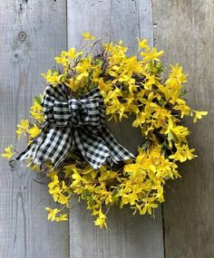 a yellow wreath with gingham ribbon hanging on a wooden fence next to flowers