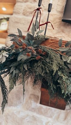 an arrangement of greenery and pine cones is hanging from a beam in front of a stone wall