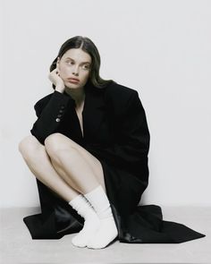 a woman sitting on the ground with her legs crossed wearing white socks and a black coat