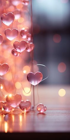 pink hearts are floating in the air near a string of lights on a table with blurry lights behind them