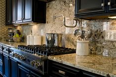 a kitchen with marble counter tops and black cabinets, along with stainless steel range hoods