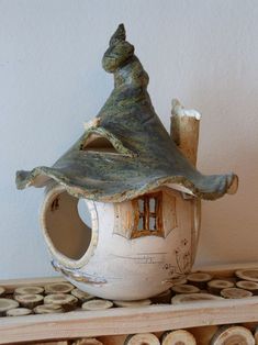 a white ceramic house with a roof and chimney on top of wood logs in front of a wall