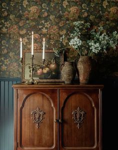 a wooden cabinet with two vases on top of it next to flowers and candles