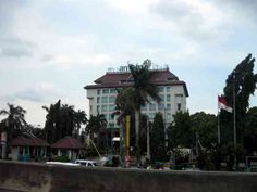 a large white building with palm trees in the foreground and cars parked on the street