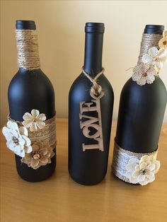 three black wine bottles decorated with flowers and twine on top of a wooden table