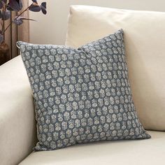 a blue and white pillow sitting on top of a couch next to a vase with flowers