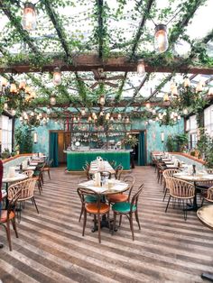 the inside of a restaurant with tables, chairs and plants hanging from the ceiling above