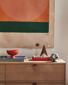 an abstract painting hangs above a dresser with books and other items on it's top