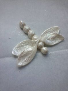 a white flower with leaves and beads is shown on a table top, ready to be used as an ornament