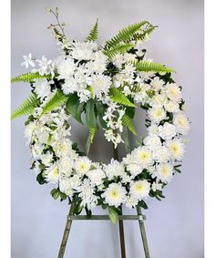 a wreath with white flowers and greenery on a easel against a gray background