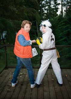 two people dressed in costumes standing on a wooden deck with trees in the back ground