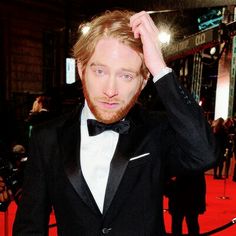 a man in a tuxedo poses on the red carpet