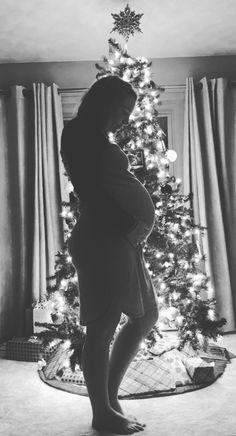 a pregnant woman standing in front of a christmas tree