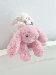 two stuffed animals sitting on top of a white shelf next to each other in front of a wall