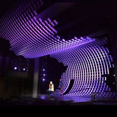 two people are standing on stage in front of a large screen that is lit up with purple lights