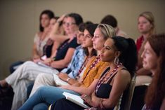 a group of women sitting next to each other in front of a crowd on chairs