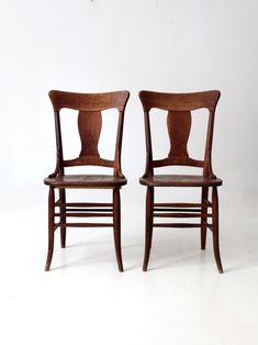 two wooden chairs sitting next to each other on a white floor with one chair facing the other