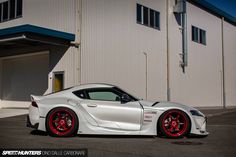 a white sports car parked in front of a building with red rims on it