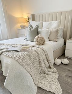 a white bed with pillows and blankets on top of it next to a night stand