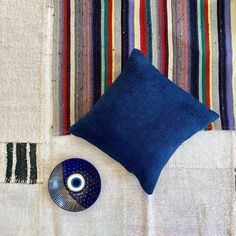 a blue pillow and a decorative bowl on a striped table cloth with a colorful wall hanging in the background