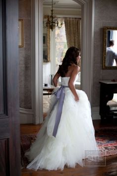 a woman in a white wedding dress standing on a rug with her back to the camera