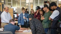 a group of people standing around a table in an office building looking at something on the desk