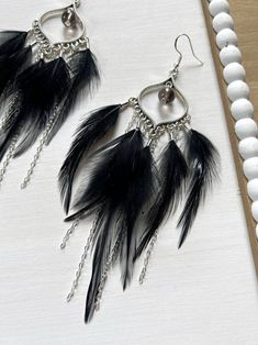 two black feathers hanging from chains on a white tablecloth next to beads and pearls