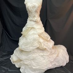 a white wedding dress is on display in front of a black backdrop and it has ruffled layers