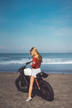 a woman sitting on a motorcycle at the beach