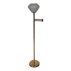 a brass floor lamp with a white glass ball on it's arm and a metal base