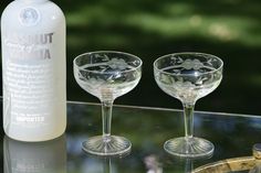 two wine glasses sitting on top of a glass table next to a bottle of alcohol