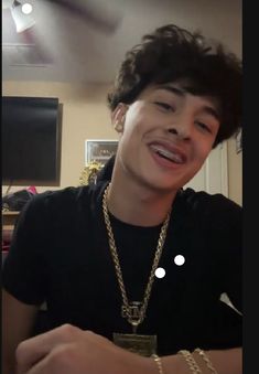 a young man wearing a black shirt and gold chain around his neck smiling at the camera