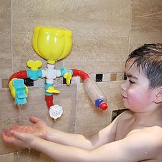 a young boy washing his hands in the bathtub with toys on the wall behind him