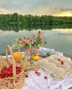 a picnic with strawberries, orange juice and fresh fruit on the table next to the water