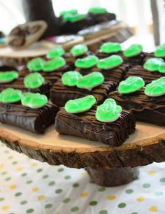 there are many pieces of chocolate cake on the wooden platter that is decorated with green icing