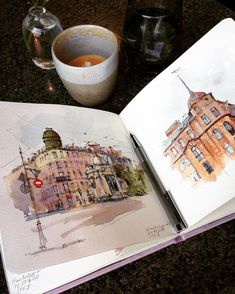 an open book with watercolors on it and a cup of coffee next to it