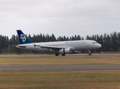 an air new zealand airplane on the runway at an airport with trees in the background