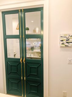 a green double door with gold trim in a white room next to a painting on the wall