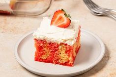 a slice of strawberry cake on a plate with a fork and glass container in the background