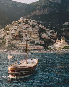 a small sailboat in the water near a city on a hill side with houses