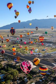 many hot air balloons are flying in the sky over a city with mountains behind them