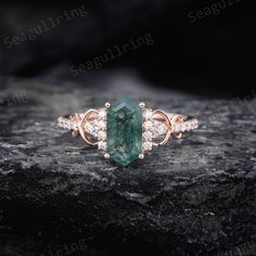 an emerald and diamond ring sitting on top of a black stone slab with white diamonds around it