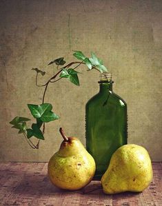 two pears sitting next to a green bottle with a plant growing out of it