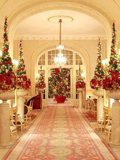 christmas trees are decorated in red and gold at the entrance to a large room with columns