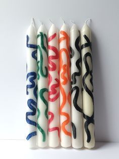 four candles with different designs on them sitting next to each other in front of a white wall