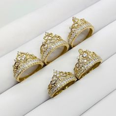 four gold rings with diamond crowns on them sitting on top of a white cloth covered box